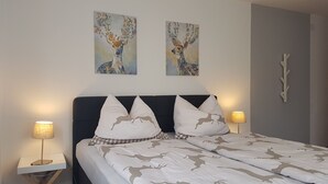 A neatly made bed with a patterned bedspread, two matching pillows, and two wall-mounted paintings of deer. There are bedside lamps on either side of the bed. - Large 105m² apartment with terrace for 4 to 6 persons & beautiful south view! (Flattach)