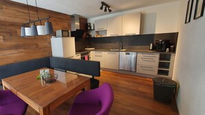 A modern kitchen with white cabinets, stainless steel appliances, and a wooden dining area with purple chairs. - Large 105m² apartment with terrace for 4 to 6 persons & beautiful south view! (Flattach)