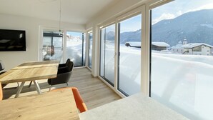 Una habitación moderna con grandes puertas correderas de vidrio, mesas de madera y vista a un paisaje nevado de montañas.