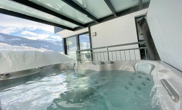 A hot tub with a glass enclosure, a metal railing, and a snowy mountain view.