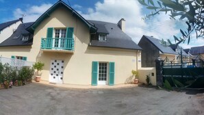 Ein zweistöckiges Gebäude mit Balkon, einer Tür und einem kleinen Gartenbereich mit Blumentöpfen.