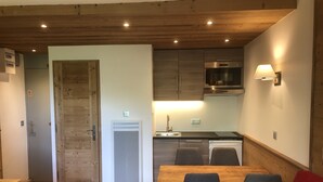 A compact kitchen with wooden cabinets, a built-in microwave, and a dining area with a table and chairs. - SKIS ON FOOTS-WIFI- GARAGE (optional) -NICE VIEW-2 ROOMS (Les Allues)