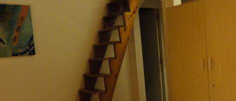 A bedroom with a wooden staircase, a bed, and a wardrobe.