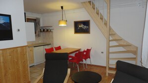 A compact living space with a dining area, kitchen, and a wooden staircase. -    Comfortable apartment in chalet with splendid view   (Allos)