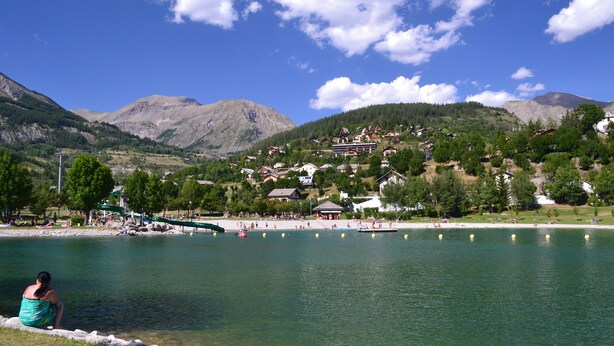 A lakeside view with a mountain backdrop, a bridge, and a cluster of houses. -    Comfortable apartment in chalet with splendid view   (Allos)