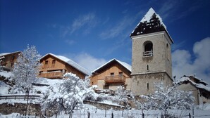 A snow-covered village with wooden houses and a prominent tower. -    Comfortable apartment in chalet with splendid view   (Allos)