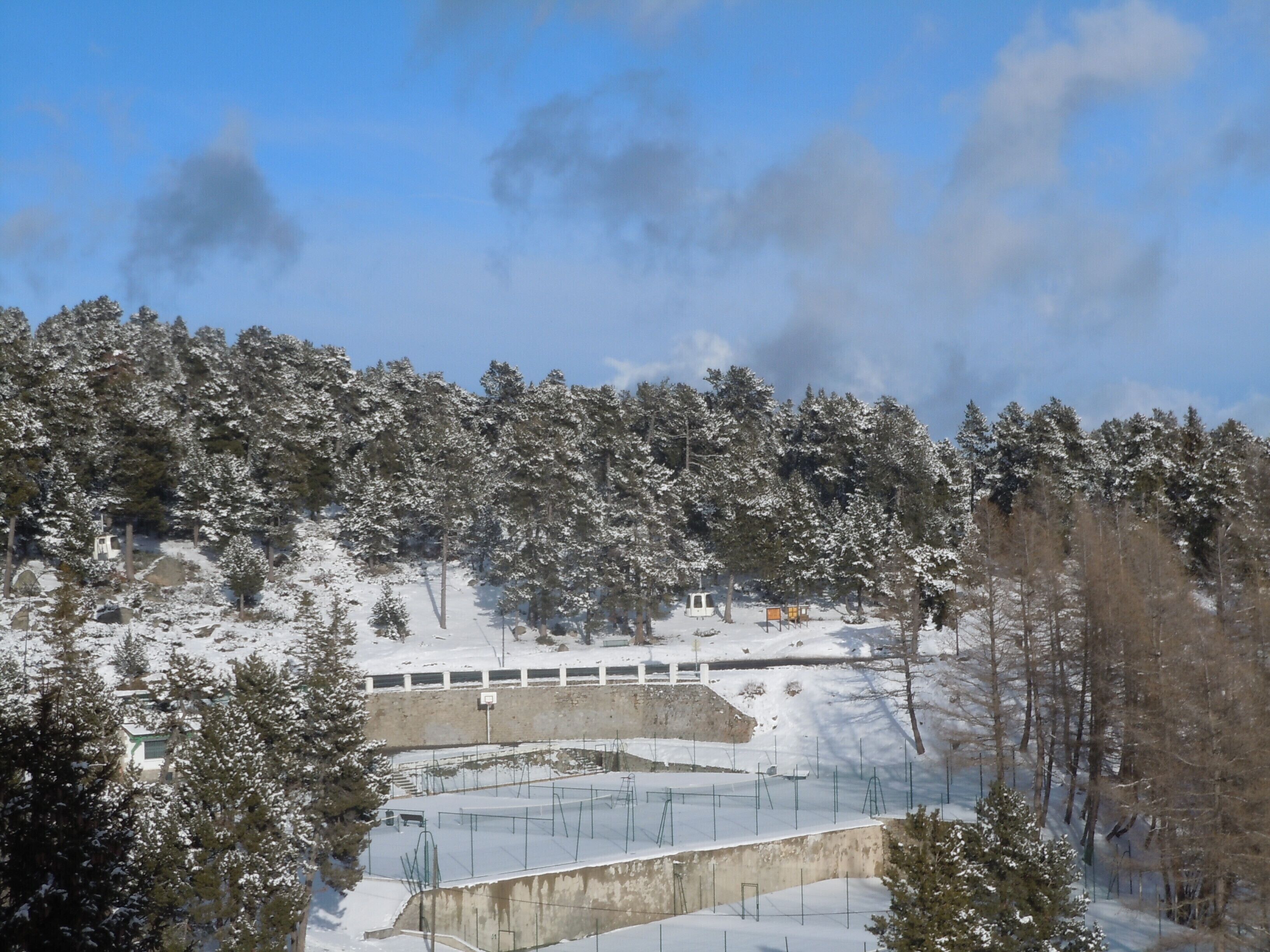 A snowy landscape with a concrete structure, possibly a viewing platform or rest area, surrounded by snow-covered trees and a clear sky.
