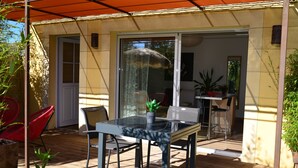 Un patio al aire libre con una mesa y sillas de vidrio, rodeado de macetas con plantas y una terraza de madera.