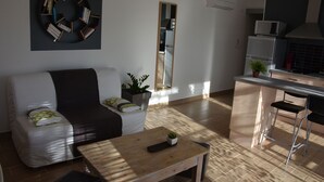 Una sala de estar moderna con un sofá, una mesa de centro y una cocina equipada con microondas y refrigerador.