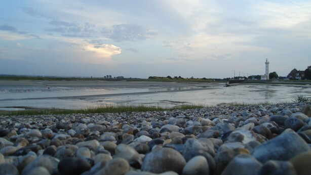 A pebbled beach with a lighthouse in the distance.