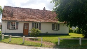 A single-story house with a tiled roof, a wooden door, and a small front yard with a fence.
