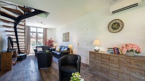 Een moderne woonkamer met een gebogen trap, een bank, een salontafel met bloemen, een houten kast en een wandklok.