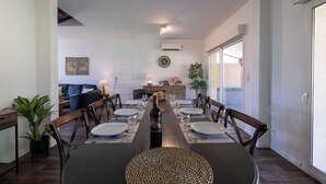 Een eetruimte met een lange tafel, gedekt voor zes personen, omringd door stoelen, met een plant en een lamp op tafel.