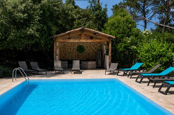 Une piscine dotée de chaises longues, une structure en mur de pierre et une végétation luxuriante tout autour.