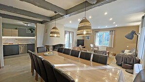 Een moderne keuken met een centraal eiland, een eethoek met een lange tafel en stoelen, en een gezellige zithoek met een bank en een lamp.