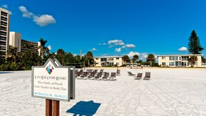 Vue d’un complexe hôtelier situé en bord de mer, avec une enseigne indiquant « Casa Mar Condo Resort ». On y voit un ciel dégagé, des palmiers et des chaises longues sur le sable.