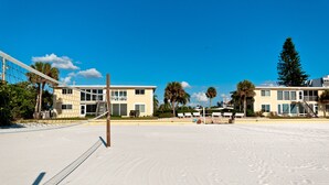 Un terrain de beach-volley avec un filet, des palmiers et des bâtiments en arrière-plan.