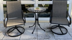 Une terrasse avec deux chaises et une table, un espace abrité offrant une vue sur une maison et des arbres.