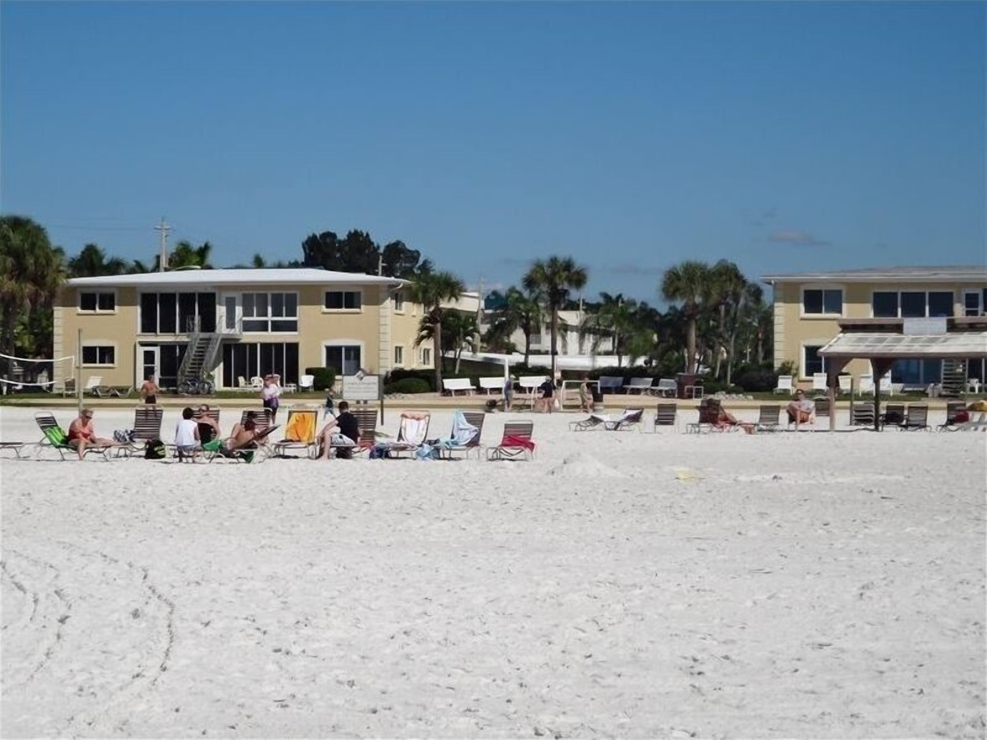 Een hotel aan het strand met meerdere verdiepingen, terras en palmbomen.