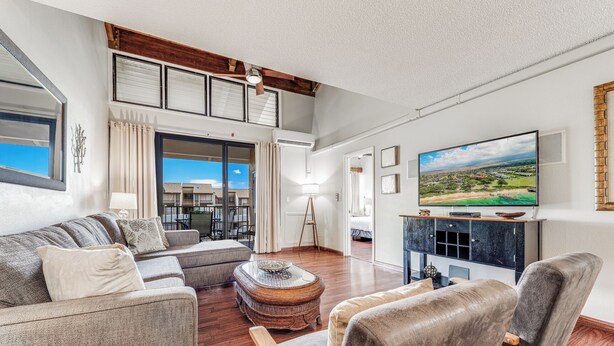 A spacious living room with a large TV, comfortable seating, and a view of the outdoors. - Large 3 Bedroom Condo Across From Beach! Pool & Hot Tub Access! Ocean View! (Kihei)