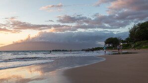 A beach with a wide sandy shore, calm water, and a few people walking along the beach. - Large 3 Bedroom Condo Across From Beach! Pool & Hot Tub Access! Ocean View! (Kihei)