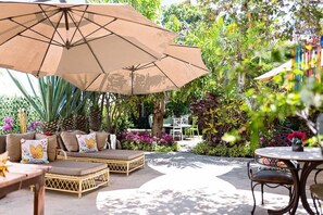 Un espacio al aire libre con patio, un sofá, sillas y una mesa bajo un paraguas grande.