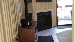 Un salon avec une cheminée, un téléviseur posé sur un meuble et une grande fenêtre.