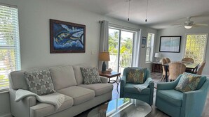 Ein Wohnzimmer mit einem beigefarbenen Sofa, zwei türkisfarbenen Sesseln, einem Glastisch und einem Bild an der Wand.