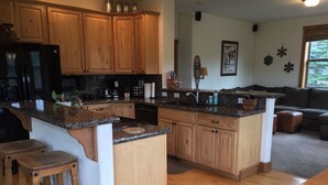 A kitchen with wooden cabinets, granite countertops, a refrigerator, and a dining area with stools. - Breckenridge Ski Area Views from 4 Bedroom, 4 Bath Home (Breckenridge)