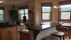 A kitchen with wooden cabinets, a granite countertop, a sink, and a dining area with stools. - Breckenridge Ski Area Views from 4 Bedroom, 4 Bath Home (Breckenridge)