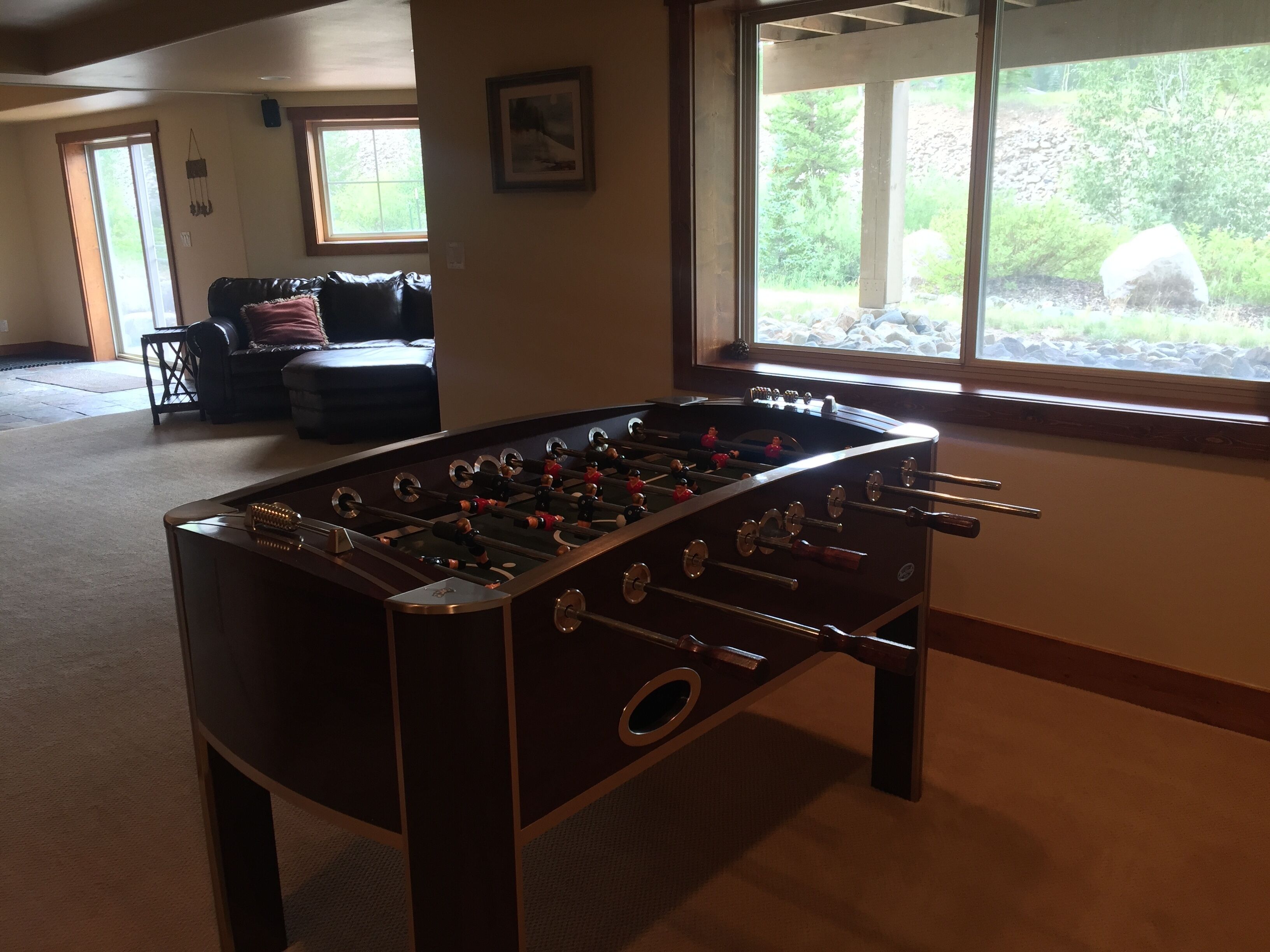 Une table de baby-foot dans une pièce dotée d’une grande fenêtre, d’un canapé et d’une porte donnant sur l’extérieur.