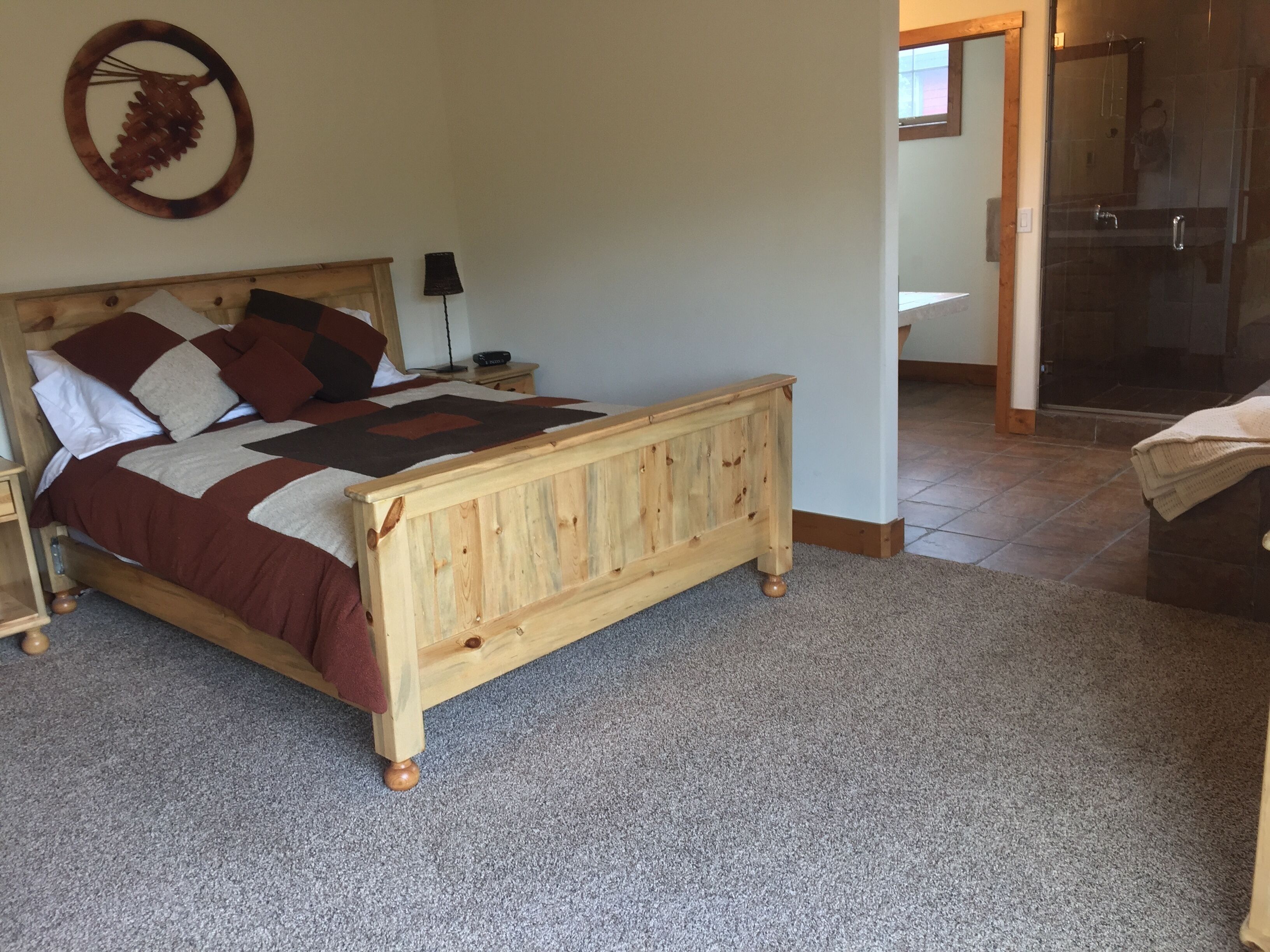 Un dormitorio con cama de madera, una mesita de noche, una lámpara y un baño visible a través de una puerta abierta.