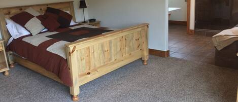 Un dormitorio con cama de madera, una mesita de noche, una lámpara y un baño visible a través de una puerta abierta.