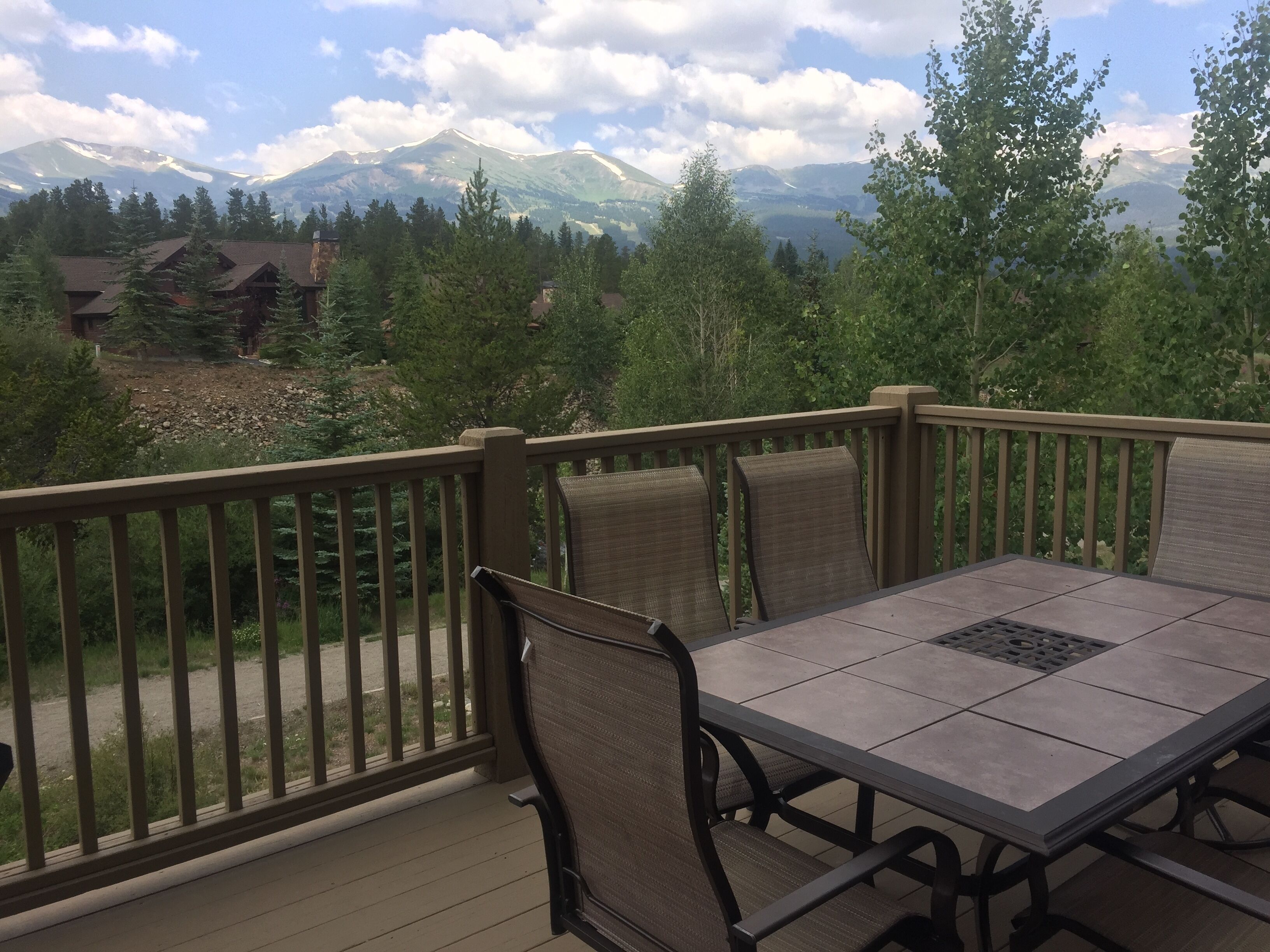 A deck with a table and chairs, overlooking a mountainous landscape with trees and buildings.