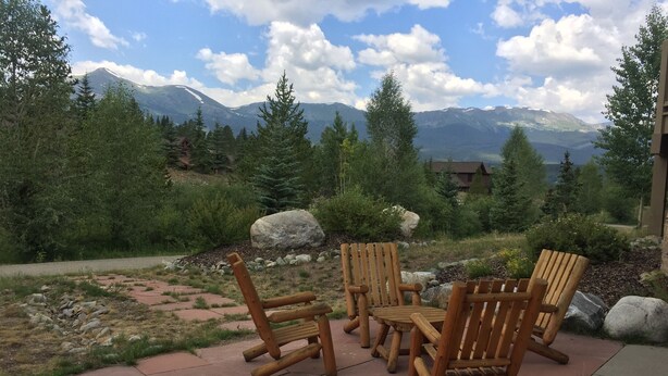 A patio with wooden chairs and a table, surrounded by rocks and greenery, with a mountain view in the background. - Breckenridge Ski Area Views from 4 Bedroom, 4 Bath Home (Breckenridge)