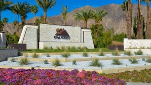 A sign for PGA WEST with a mountain logo, surrounded by palm trees and a landscaped garden. - Luxury Lake Front PGA West Golf Course View Townhome / Private Spa / Adults Only (La Quinta)