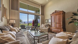 A spacious living room with a large window, a glass coffee table, and a wooden cabinet. - Luxury Lake Front PGA West Golf Course View Townhome / Private Spa / Adults Only (La Quinta)