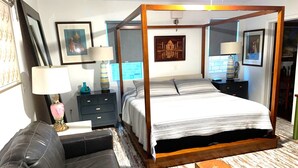 Une chambre à coucher avec un lit à baldaquin, un canapé en cuir noir, une petite table ronde avec un livre et une table de chevet avec une lampe.