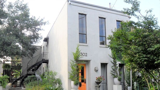 Un bâtiment à deux étages, de couleur blanche, portant le numéro 302, avec un petit jardin à l’avant agrémenté de plantes en pot et un chemin menant à l’entrée.