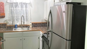 Une cuisine avec des meubles blancs, un réfrigérateur en acier inoxydable, une cuisinière et une fenêtre avec un rideau.
