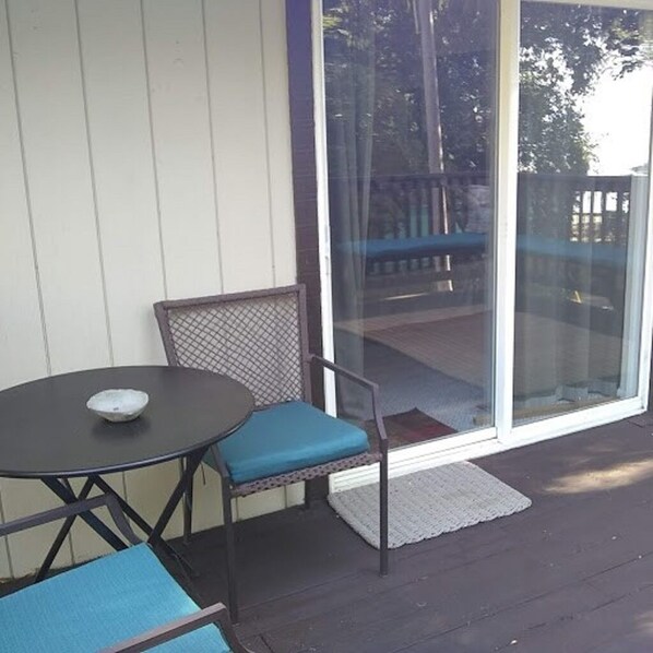 A covered outdoor area with a table and two chairs, a glass door leading outside, and a wooden deck visible through the door.