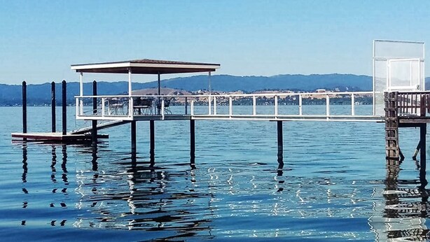 Une jetée s’avançant dans une étendue d’eau calme, avec un espace de repos abrité et un petit bâtiment à son extrémité.