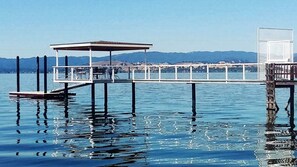 A pier extending into calm water with a covered seating area and a small building at the end.