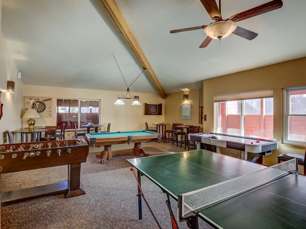 A recreational room with a foosball table, pool table, ping pong table, and ceiling fan.
