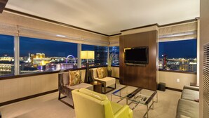 A hotel room with a city view, a flat-screen TV, a sofa, a glass coffee table, and a chair.
