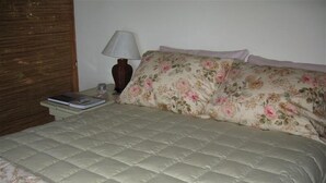 Een bed met een bloemenbedekking, een nachtkastje met een lamp en een boek.