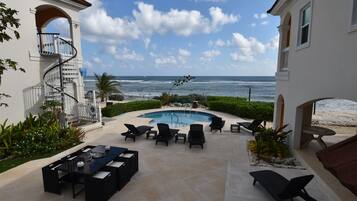 Uma área de piscina com espreguiçadeiras e uma mesa de jantar, com vista para o oceano.