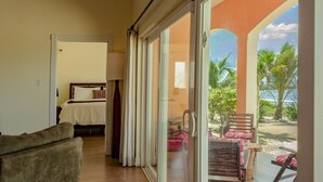 Ein Hotelzimmer mit einer großen Schiebeglastür, die auf einen Balkon mit Blick auf Palmen und den Strand führt.