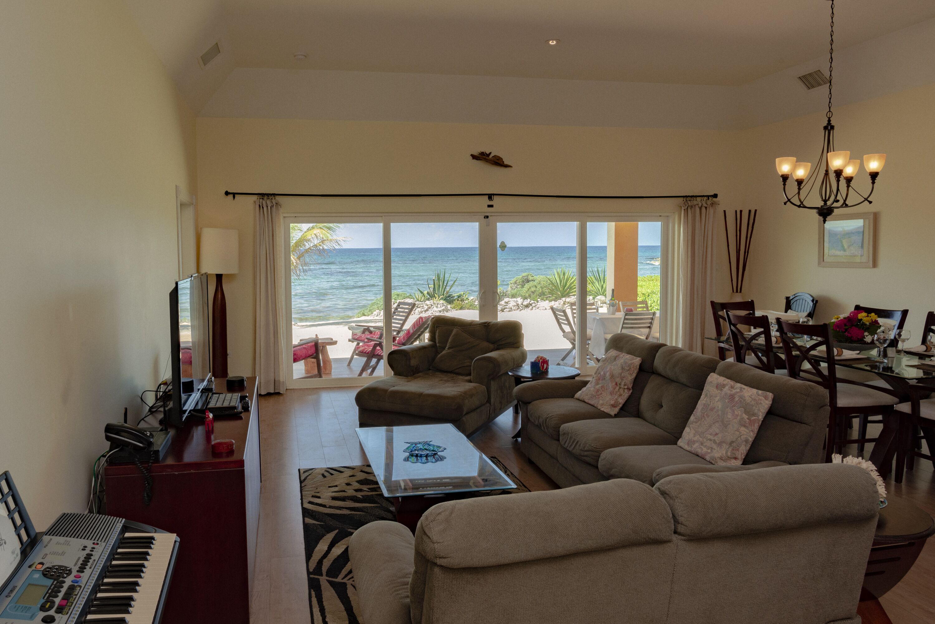 A living room with a view of the ocean, a piano, and a dining area with chairs and a table.