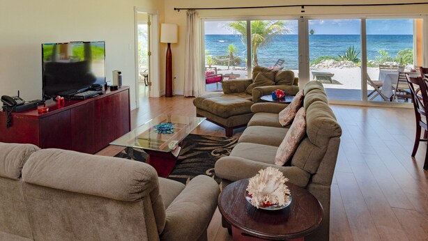 Ein Wohnzimmer mit großem Flachbildfernseher, einer Couch, einem Couchtisch und Meerblick durch große Schiebetüren.